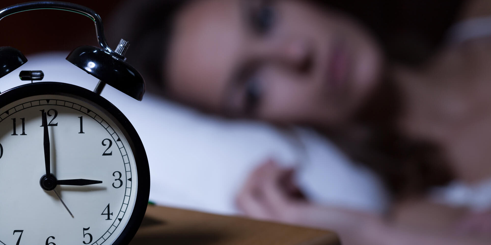 woman lying on bed and looking alarm clock