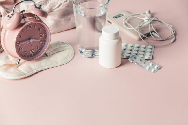 A water glass, Pink alarm watch and tablets in a pink background